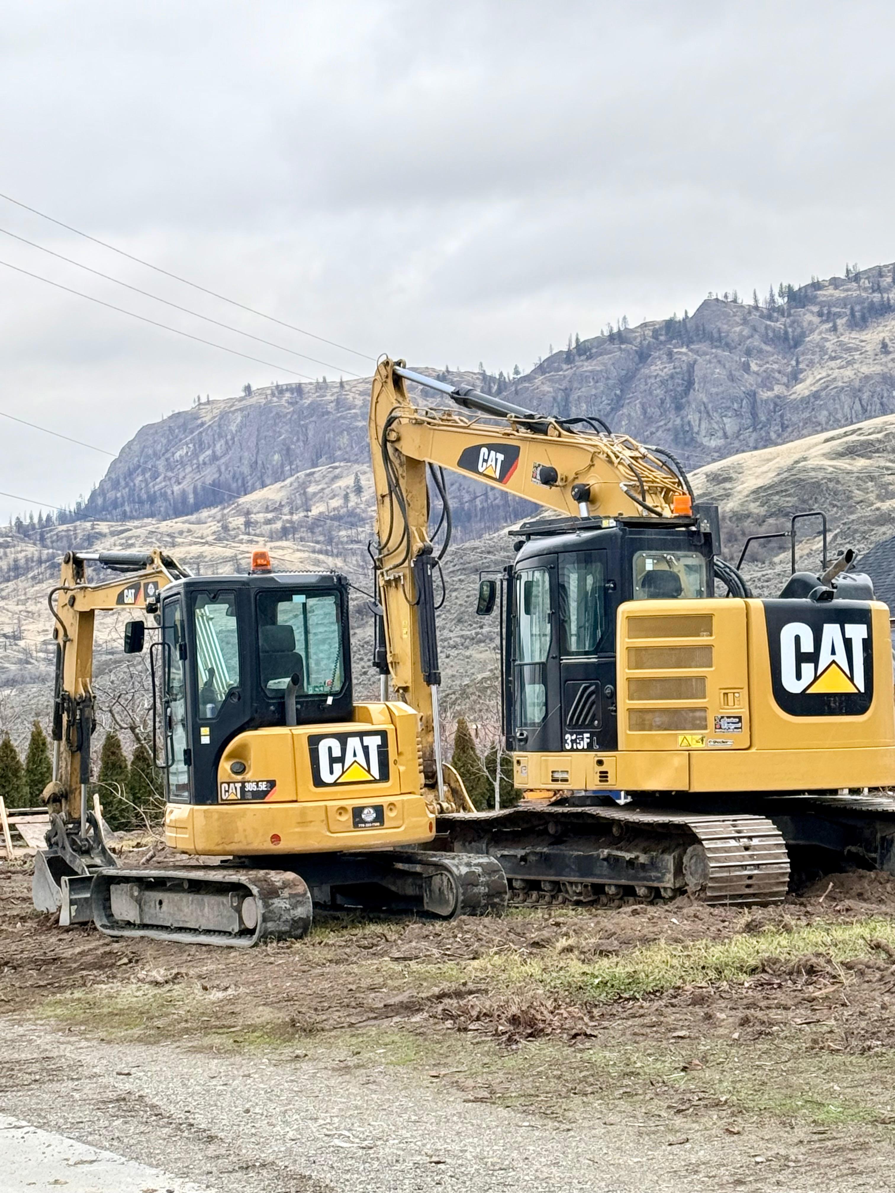 Two CAT excavators with South Okanagan mountains in the background
