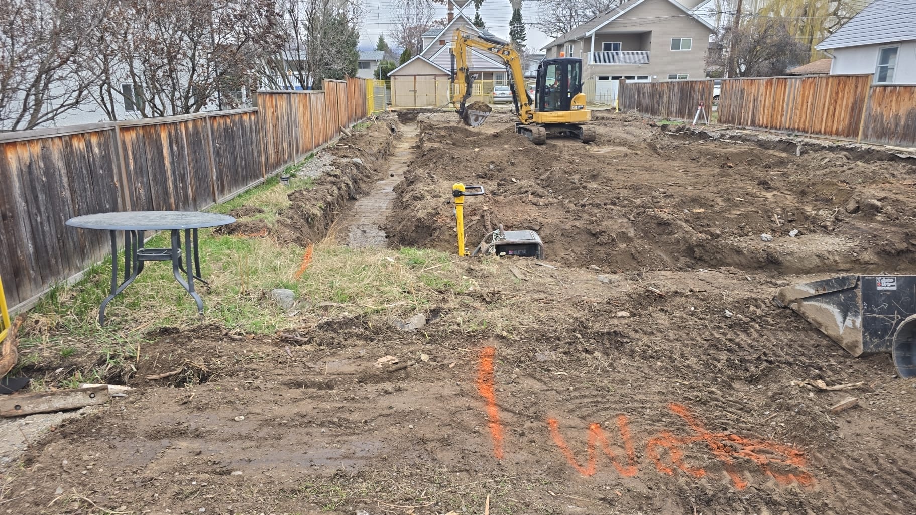 CAT excavator digging a trench in a residential backyard in Oliver BC